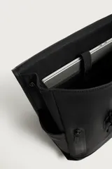 Mochila de diseño minimalista en acabado engomado color negro. Cuenta con compartimento principal con cierre de solapa y hebilla de liberación rápida, bolsillo frontal con cierre, compartimento interno para dispositivos electrónicos y espalda acolchada con banda de sujeción para equipaje.