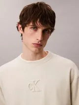 Sweater de punto color beige con cuello redondo, mangas largas y corte regular. Cuenta con el logo distintivo de Calvin Klein bordado en relieve al tono en el pecho.