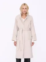 Tapado largo color beige con cuello solapa, cinturón y mangas largas con detalle matelassé.