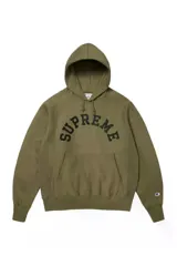 Hoodie de algodón color verde oliva con capucha y bolsillo tipo canguro. Presenta el logo de Supreme bordado en el pecho con tipografía arqueada y el logo de Champion bordado en la manga izquierda.