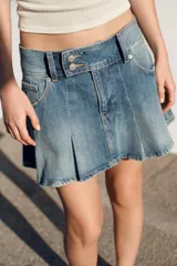 Falda mini de jean con diseño de tablas, tiro medio, bolsillos delanteros y cierre frontal con botones.