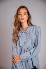 Camisa celeste con cuello con volados y lazos, mangas largas con puños elásticos y corte holgado.