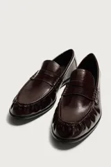 Mocasín de vestir negro de estilo clásico con detalle de antifaz en la parte superior, suela a tono y ligero tacón.