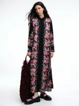 Vestido camisero largo de algodón negro con cuello camisero, cierre frontal de botones y mangas largas. Presenta un diseño con bordados florales coloridos a lo largo de toda la prenda.