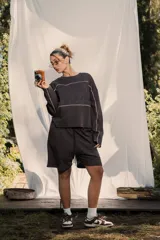 Buzo crewneck color chocolate, de tela rústica liviana, con estampado en el frente y la espalda. Presenta líneas blancas decorativas en el pecho y los brazos, y bordes deshilachados en los puños y el dobladillo.