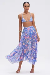 Falda larga de playa con silueta fluida y movimiento ligero, confeccionada en tela semitransparente con estampado floral en tonos azules y rosados.
