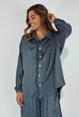 Camisa celeste de seda con botones blancos y detalle de flecos en el frente. Corte holgado y mangas largas con puños abotonados.