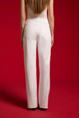 Pantalón jean blanco de corte flare y tiro alto, con detalles de tachas a lo largo de las costuras laterales y botamanga sin costura.