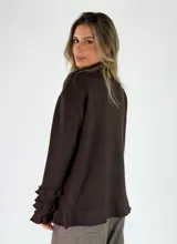 Saco de punto negro con cierre frontal, manga larga con volados en los puños y detalles de volados en el cuello y el ruedo.
