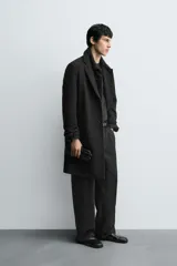 Abrigo de corte regular fit confeccionado en tejido compacto con mezcla de lana. Presenta cuello con solapas de muesca, cierre frontal de botonadura, bolsillos de vivo en la cadera y abertura central en la espalda.