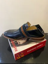 Mocasín de cuero color beige con textura reptil, detalle de tira ancha horizontal y suela de madera.