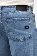 Jean de corte mom fit en color azul medio con acabado marmolado, confeccionado en denim resistente. Presenta cierre frontal con botón, bolsillos laterales y traseros, y un ajuste ligeramente holgado en las piernas con terminación recta.