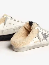 Zapatilla deportiva de cuero blanco con cordones grises, detalle de estrella plateada con glitter en el lateral y forro de lana color crema.