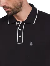 Polo de manga corta negra con cuello clásico, tapeta con botones y logo de pingüino bordado en el pecho. Presenta ribetes blancos en cuello y mangas.
