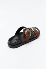 Sandalia tipo slide color tostado, con doble tira ancha y hebillas metálicas plateadas con diseño texturado. Su base es ergonómica y liviana, de color negro.