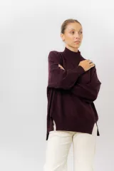 Sweater de tejido de punto color beige, con cuello alto, hombros caídos, mangas largas con puños acanalados y tajos laterales en el ruedo.