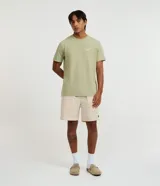 Bermuda de sarga color beige, de corte recto, con cintura elástica y cordón ajustable. Cuenta con bolsillos laterales y un discreto parche con logo aplicado en el dobladillo inferior.