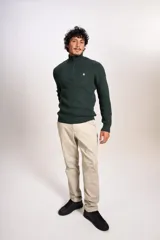Sweater de punto acanalado en color verde oscuro, con cuello alto y cierre frontal parcial de un cuarto. Presenta puños y ruedo elásticos, con el logo de la marca bordado en el pecho.