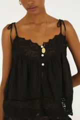 Blusa color blanco off-white, confeccionada en algodón con detalles de encaje floral en el escote y en el ruedo, tirantes finos ajustables con lazo y cierre frontal con pequeños botones.