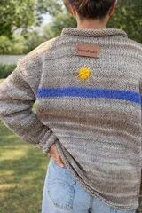 Sweater de punto en tonos beige con efecto degradado, cuello redondo y manga larga. Presenta una franja horizontal en color azul y el bordado de las letras 'SM' en color rojo en el pecho.