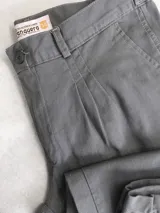 Bombacha de campo gris con trabillas para cinturón, bolsillos laterales y pliegues en el frente.