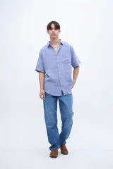 Camisa de manga corta color celeste claro, con cuello solapa clásico y bolsillo en el pecho. Presenta una textura ligera y un calce regular.