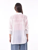 Camisa blanca traslúcida con rayas verticales doradas, de corte holgado, manga 3/4 y bolsillo en el pecho.