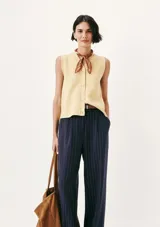Chaleco de punto sin mangas en color amarillo suave, con cuello en V y cierre frontal de botones al tono. Presenta un diseño clásico y minimalista con un pequeño bordado decorativo en la parte inferior.