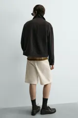 Bermuda de algodón color beige claro, de corte relajado y largo hasta la rodilla. Presenta cierre frontal con cremallera y botón, bolsillos delanteros y bolsillo cerillero, además de bolsillos traseros de plastrón.