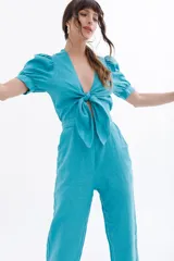 Mono negro de lino con escote pronunciado en V y nudo frontal que deja ver un corte en la cintura. Mangas cortas abullonadas y pantalón de corte recto.