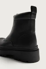 Bota de caña media con cierre frontal mediante cremallera, confeccionada en material con textura. Presenta horma redonda y suela de goma con volumen y piso track.
