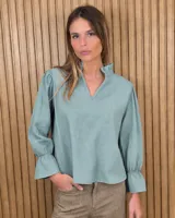 Blusa de algodón color azul, de corte suelto, con mangas largas abullonadas y cuello con volados y escote en V.