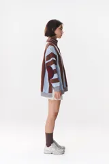 Buzo de tejido de punto con diseño de rayas verticales en tonos bordó y rojo. Presenta cuello alto con cierre frontal, mangas largas con coderas en contraste y detalles de costuras visibles.