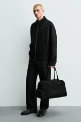 Bolso de viaje de diseño minimalista confeccionado en piel con acabado serraje. Cuenta con compartimento principal con cierre de cremallera e imanes, interior con bolsillos organizadores y doble asa de mano en piel.