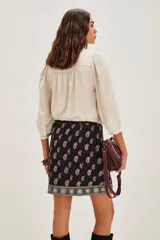 Falda corta negra estilo wrap con estampado paisley en tonos rojo y blanco. Presenta un borde decorativo con motivos circulares en tonos plateados y beige.