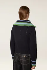 Cárdigan de punto azul marino con cierre frontal de cremallera. Presenta cuello tipo camionero y puños con detalles de rayas en tonos verde y celeste. El tejido tiene una textura acanalada con detalles calados decorativos.