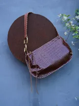 Cartera de cuero crocco con herrajes en bronce, silueta curva, terminación artesanal en los bordes y correa de hombro ajustable con detalles metálicos.