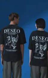 Remera de algodón premium con efecto nevado, corte oversize y cuello redondo. Presenta una estampa gráfica en color blanco en la espalda que incluye la palabra 'DESEO', una ilustración de una rosa y una figura alada, junto con frases poéticas.