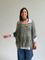 Sweater de punto color verde oliva con diseño de paneles horizontales de encaje floral, corte holgado y mangas tres cuartos. Incluye una bufanda del mismo tono y tejido, y se presenta superpuesto sobre una camisa blanca de cuello clásico.