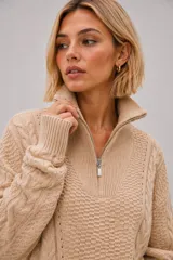 Sweater de punto grueso color beige, con diseño de trenzas y textura, cuello alto con cierre metálico frontal y calce oversize.