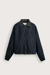Cazadora de corte relajado confeccionada en tejido denim de algodón sin lavados, con ligero acolchado interior. Presenta cuello solapa en tejido efecto piel a contraste, cierre frontal de cremallera, bolsillos de vivo en la cadera y puños elásticos.