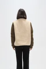 Campera de diseño híbrido que combina paneles de corderito sintético en color crema con mangas y bolsillos de tela técnica acolchada en color verde militar. Presenta cierre frontal completo, cuello alto y un pequeño parche decorativo en el pecho.