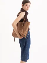 Bolso tipo tote de cuero color tostado con doble asa de hombro, detalles de hebillas metálicas en el frente y cierres laterales decorativos.