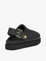 Zueco de la marca UGG modelo Goldenstar, confeccionado en cuero nobuck negro. Presenta una suela de plataforma de EVA ultra liviana y una correa trasera ajustable con hebilla metálica dorada.