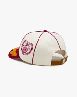 Gorra de béisbol de cinco paneles color blanca con visera color bordó. Presenta un parche frontal de fieltro con la inscripción "NUDE Project" y bordados de hojas en la visera en color amarillo mostaza.