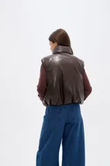 Chaleco acolchado de cuero sintético en color marrón oscuro, con cuello alto, cierre frontal y diseño holgado.