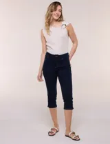 Pantalón capri de jean azul con calce ajustado, tiro alto, cinco bolsillos, cierre frontal con botón y pequeños tajos en los ruedos.
