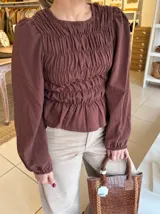 Blusa color chocolate con diseño de frunces elásticos en el frente y la espalda, mangas largas abullonadas con puños elásticos y corte peplum.