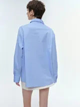 Camisa oversize de popelina de algodón con diseño de rayas verticales, cuello clásico, cierre frontal con botones, manga larga con puños anchos y bolsillo aplicado en el pecho.