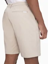 Bermuda color beige de corte recto. Confeccionada en tejido de algodón elástico. Cuenta con bolsillos laterales y traseros, cierre con cremallera y botón, trabillas para cinturón e insignia con el logo de Calvin Klein.